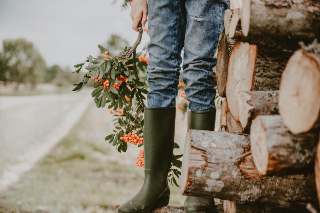 person in rain boots standing by chopped firewood, off-grid living