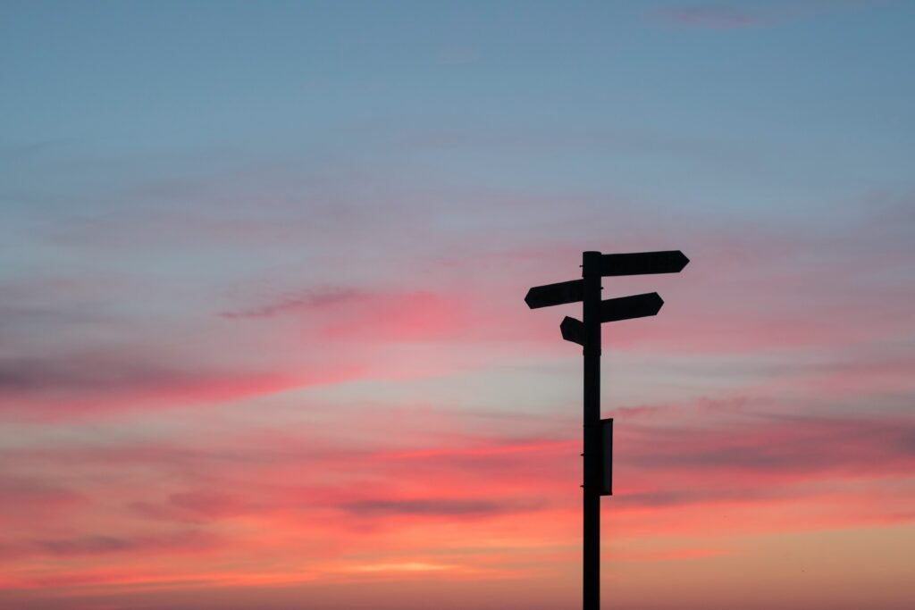 signpost silhouette against sunset sky, choosing a different way of living